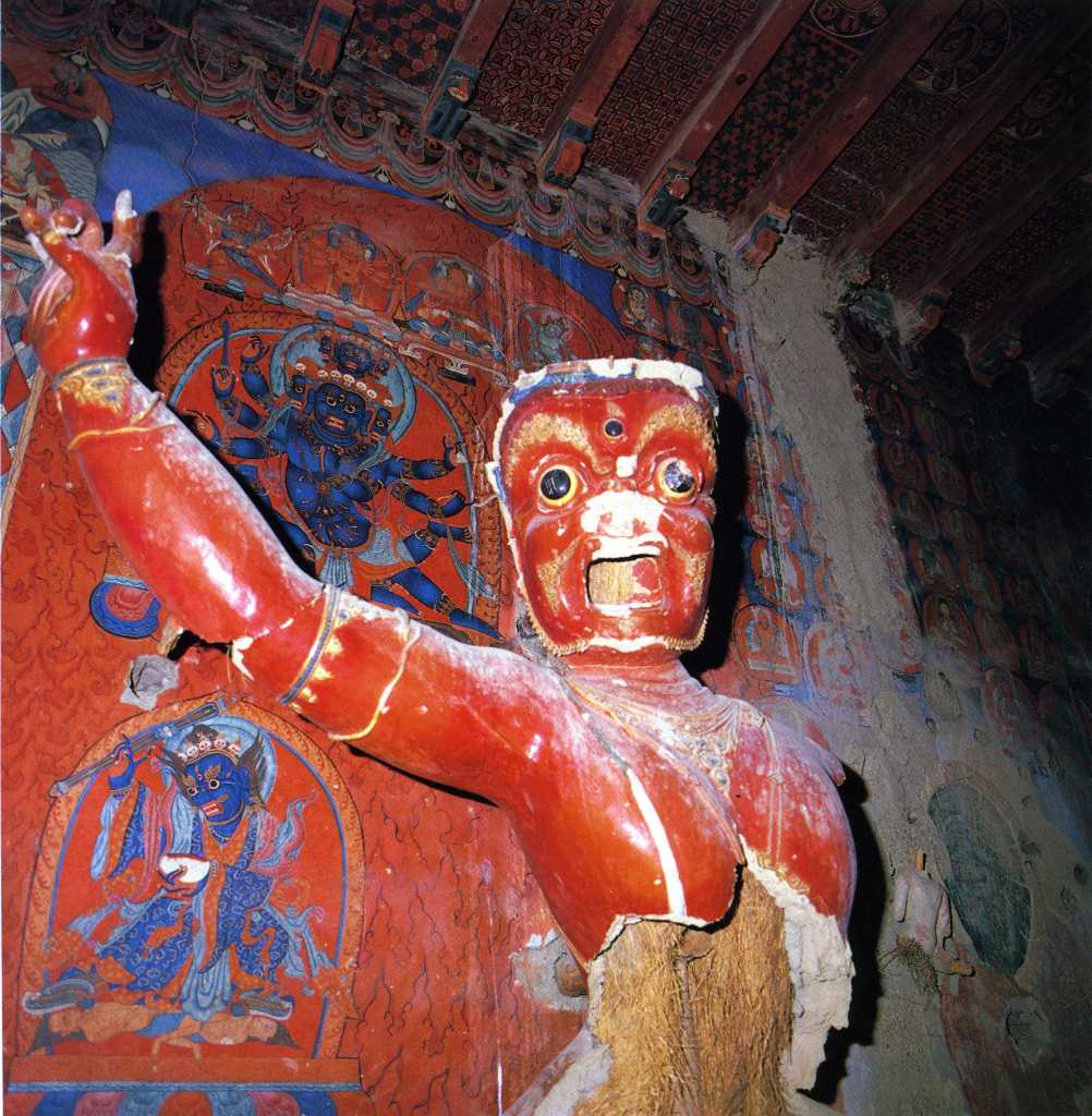 Tibet Guge 06 Tsaparang White Temple 02 01 Hayagriva Immediately on the left of the door is a 5m-high terrific image of red Hayagriva (Tib. Tamdrin), looking at us with its three wide open eyes. Hayagriva used to have a horse head emerging from his hair, and his right hand would have held a vajra. As the guardian of the door, Hayagriva is portrayed at the entrance to the temple to keep away evil influences and to protect the sanctity of the place. Photo - Weyer/Aschoff: Tsaparang, Tibets Grosses Geheimnis.